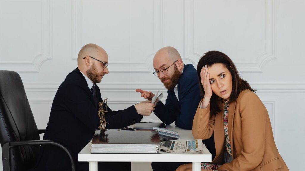 Two lawyers discuss documents with a worried client in a professional office setting.