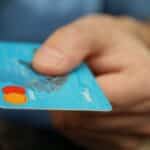 A close-up shot of a hand offering a blue debit card for payment.