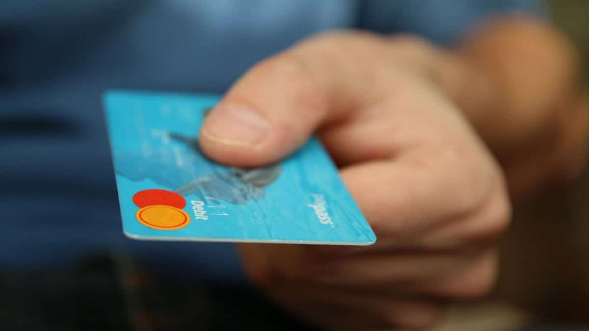 A close-up shot of a hand offering a blue debit card for payment.