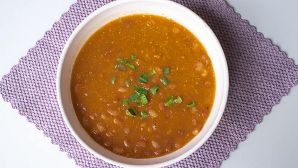 Hearty homemade bean soup garnished with green onions served in a white bowl.