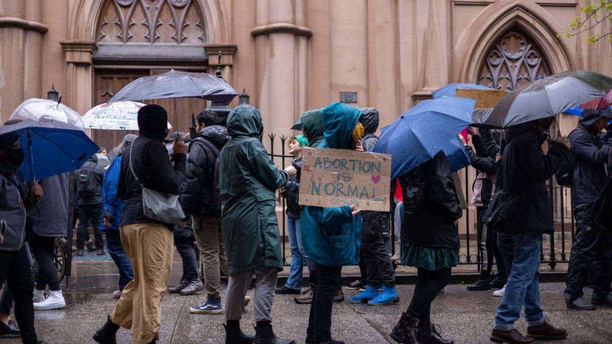 Activists protest for abortion rights in a rainy New York street. Umbrellas and placards visible.