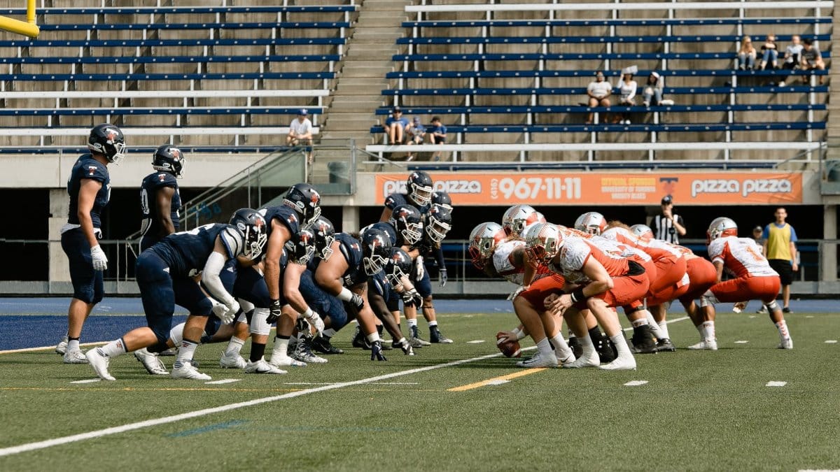 American football teams in a stand-off on a Toronto field, capturing tension.