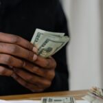 Adult counting dollar bills at a desk, focused on money management and finance.
