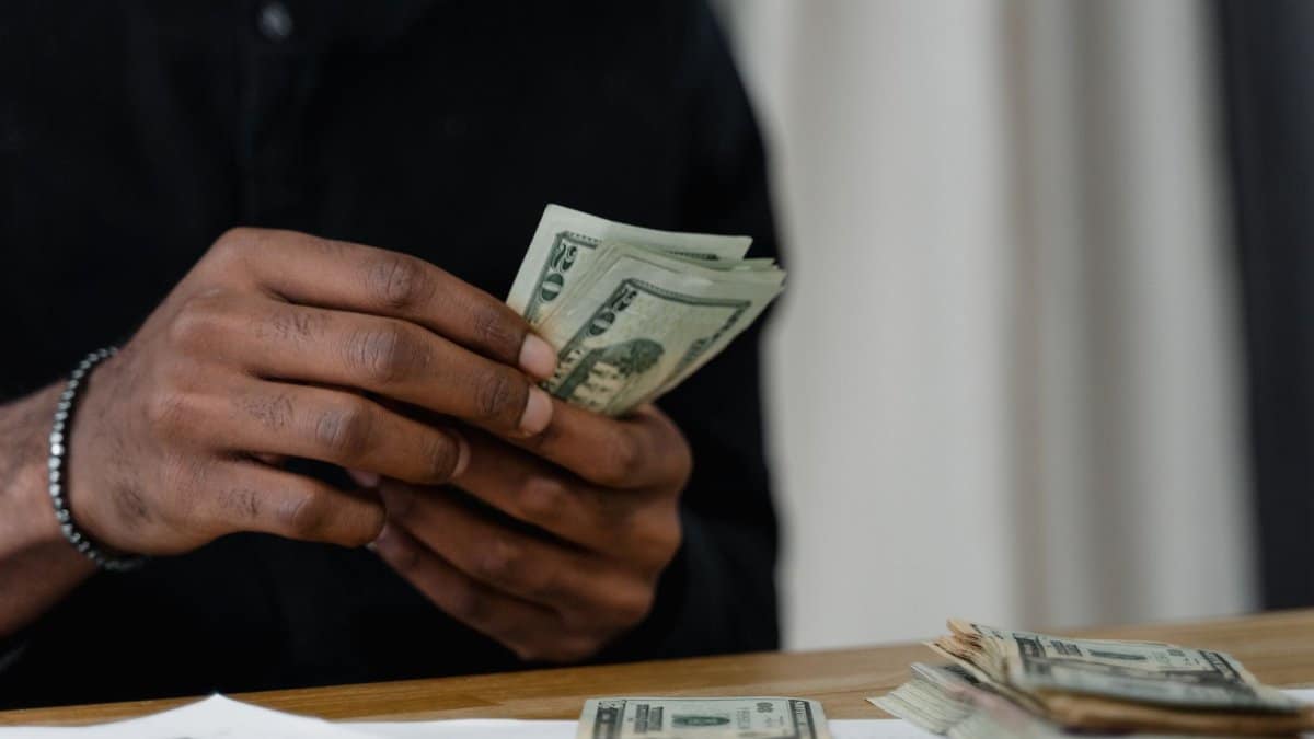 Adult counting dollar bills at a desk, focused on money management and finance.