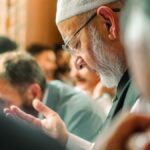 An elderly Muslim man in a mosque praying with others during a religious gathering.