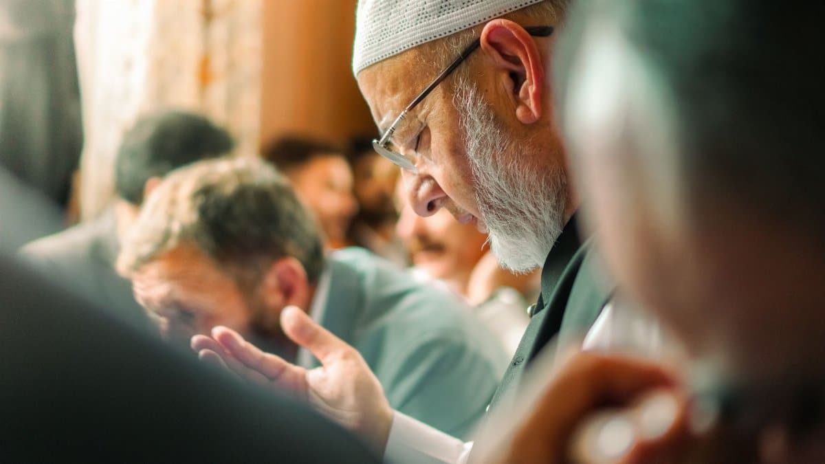 An elderly Muslim man in a mosque praying with others during a religious gathering.