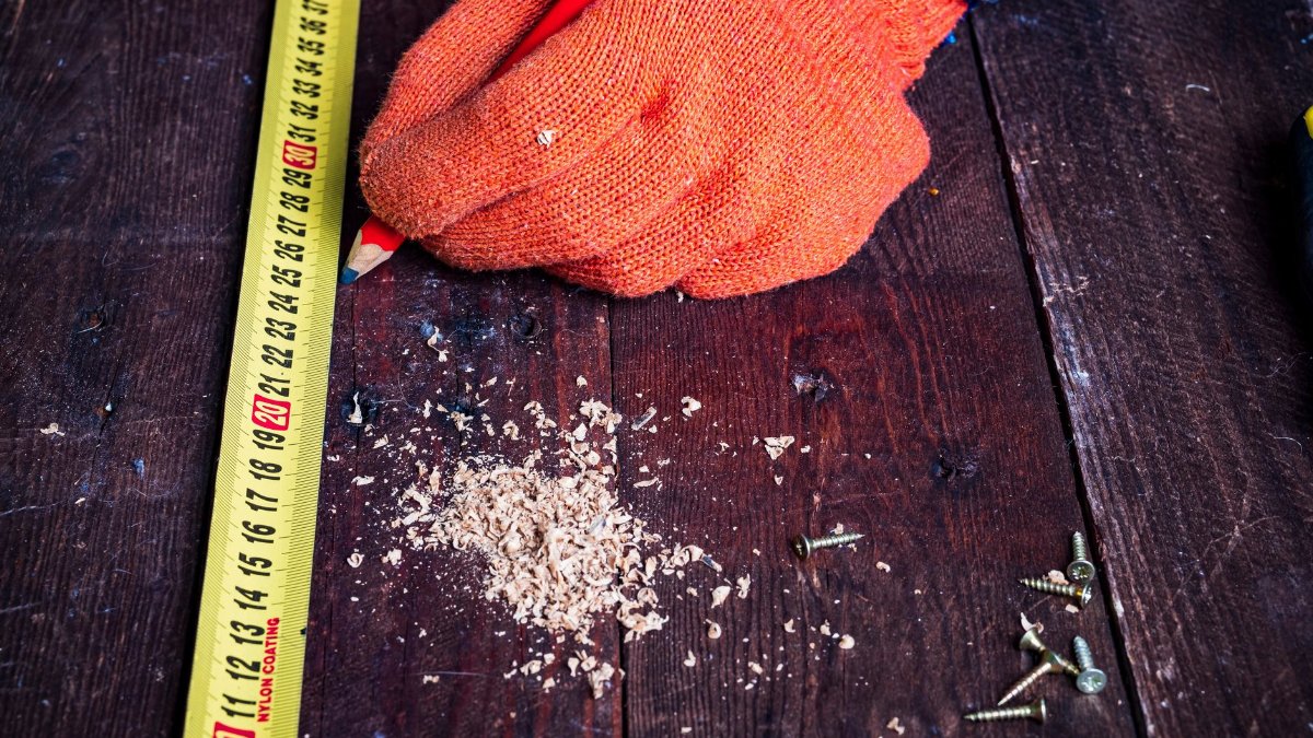 Carpenter measuring wood with measuring tape, pencil, and screws on workbench.