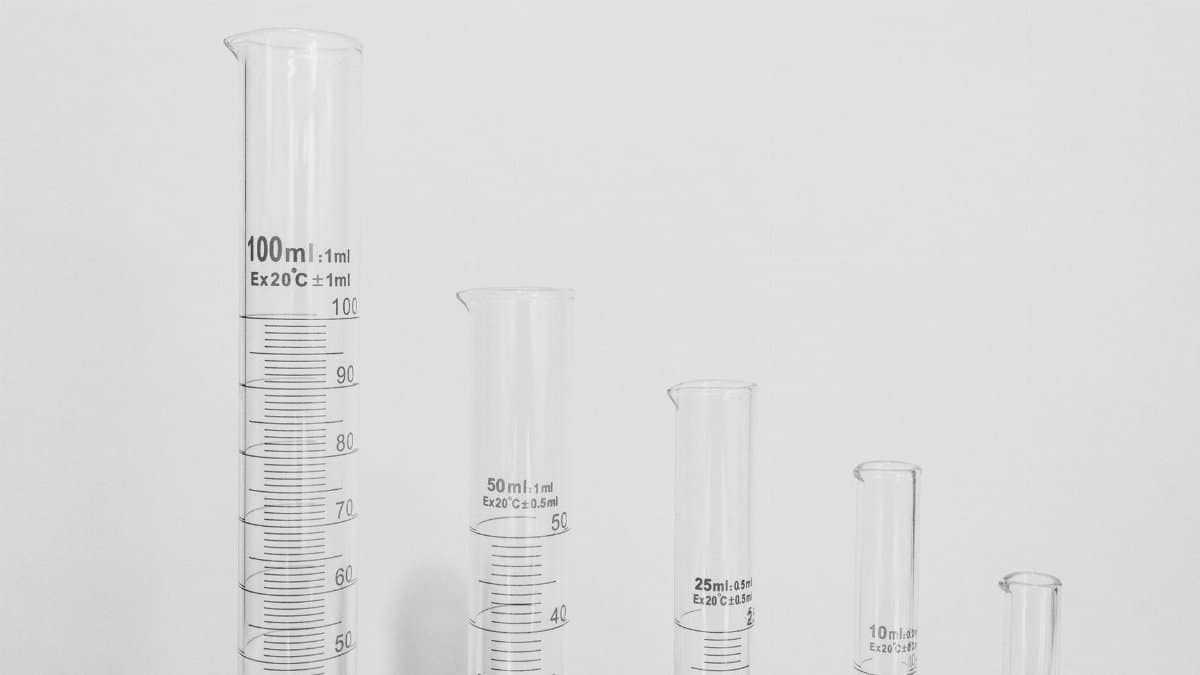 Close-up of various laboratory glassware including test tubes and measuring cylinders on a white background.