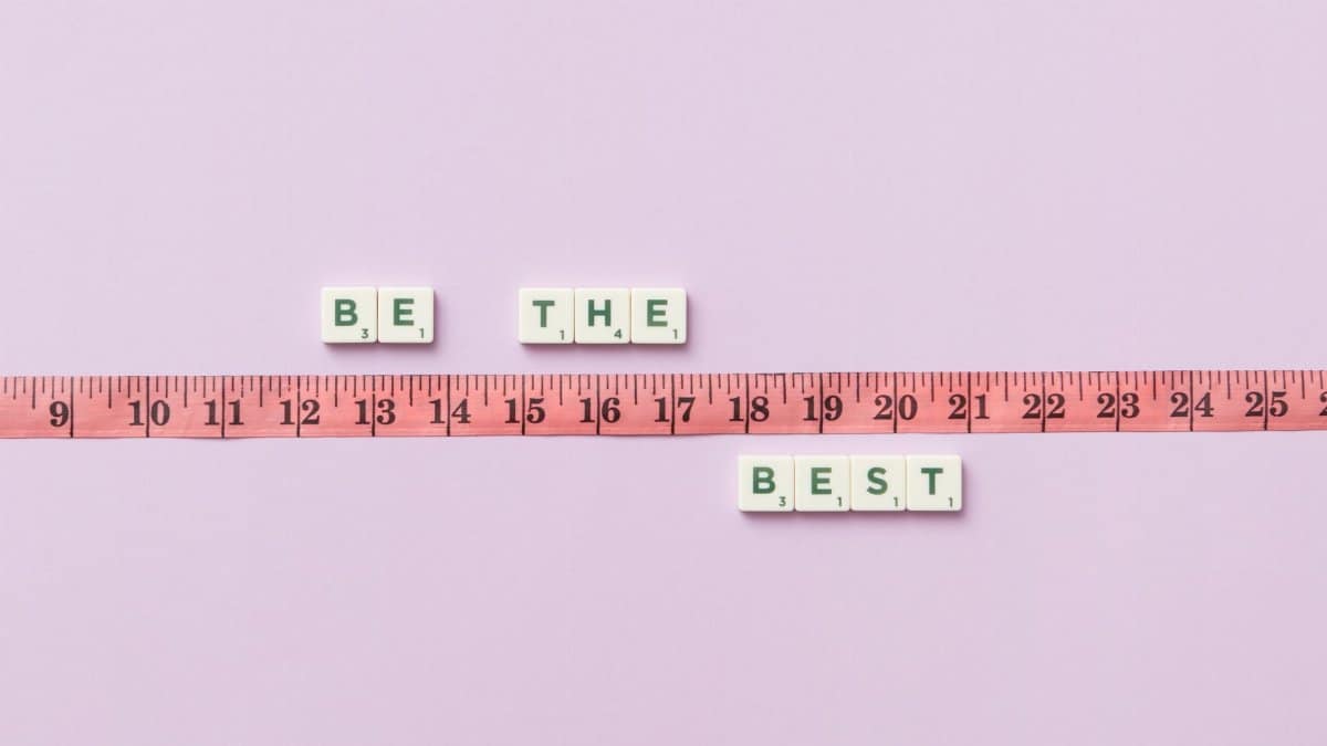 Scrabble tiles spell 'Be the Best' next to a measuring tape on a pastel background.