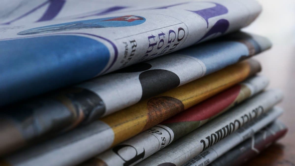 Close-up of a stack of colorful newspapers on a wooden table, showcasing print media.