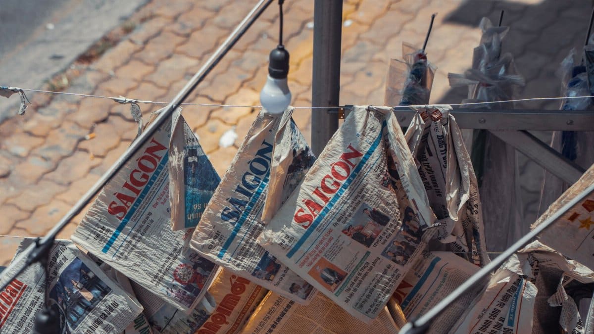Outdoor scene of hanging newspapers, featuring Saigon headlines, offering a glimpse of urban life.