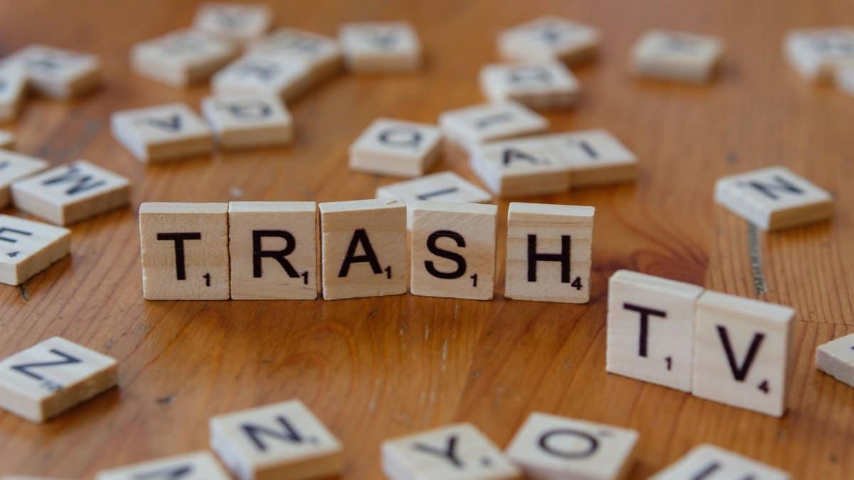 Scrabble tiles on a wooden surface spelling out 'Trash TV', conveying media critique.