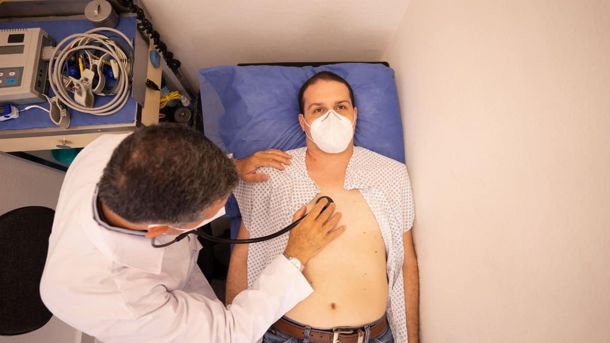 Doctor in protective mask examines patient with stethoscope in medical clinic.