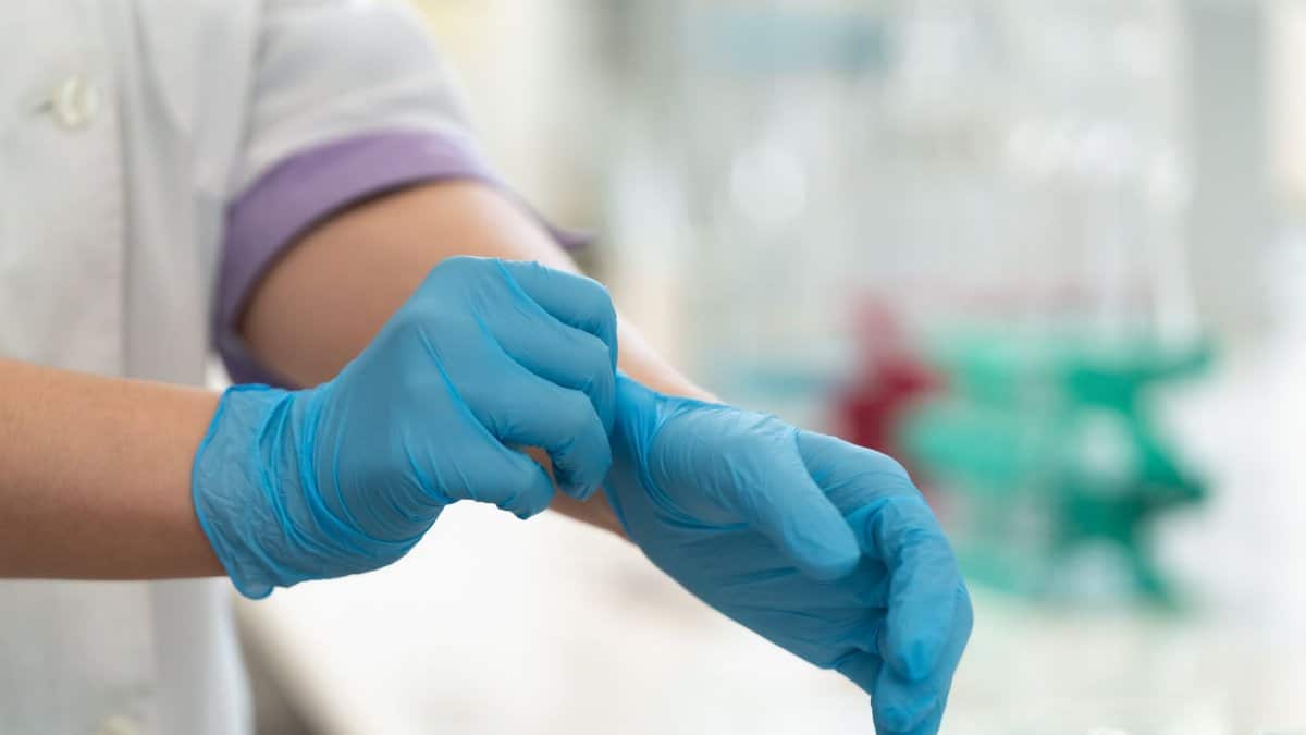 Close-up of hands wearing blue medical gloves in a laboratory setting.