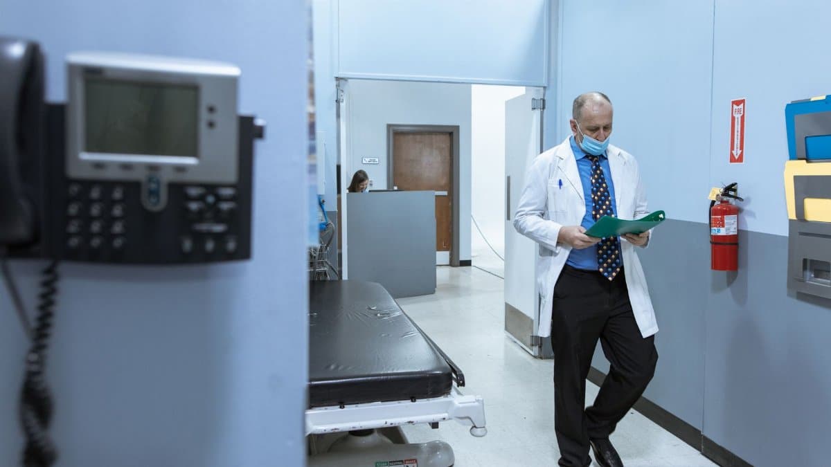 A doctor in a lab coat reads medical files in a hospital hallway, illustrating professional healthcare settings.