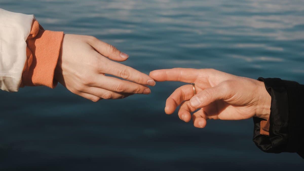 Close-up of two hands reaching across water, symbolizing connection and intimacy.
