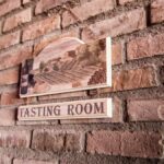A quaint tasting room sign on a rustic brick wall creates a vintage ambiance.