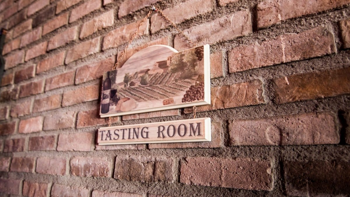 A quaint tasting room sign on a rustic brick wall creates a vintage ambiance.