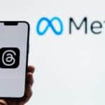 A hand holding a smartphone showing the Threads app with Meta logo in the background.