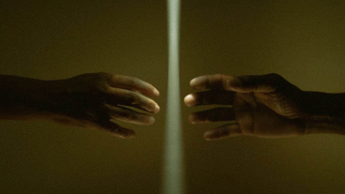 Two hands reaching toward each other through a beam of light, concept of connection and distance.