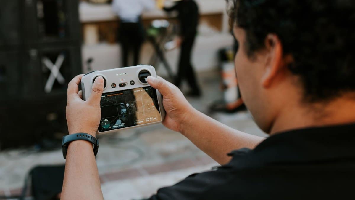 A man with short hair operating a drone controller at an outdoor event, focused on the screen.