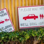 Car retrieval signs near a wall with plants in a waiting area.