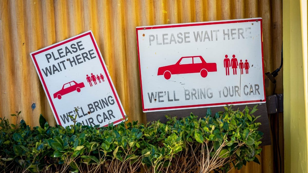 Car retrieval signs near a wall with plants in a waiting area.