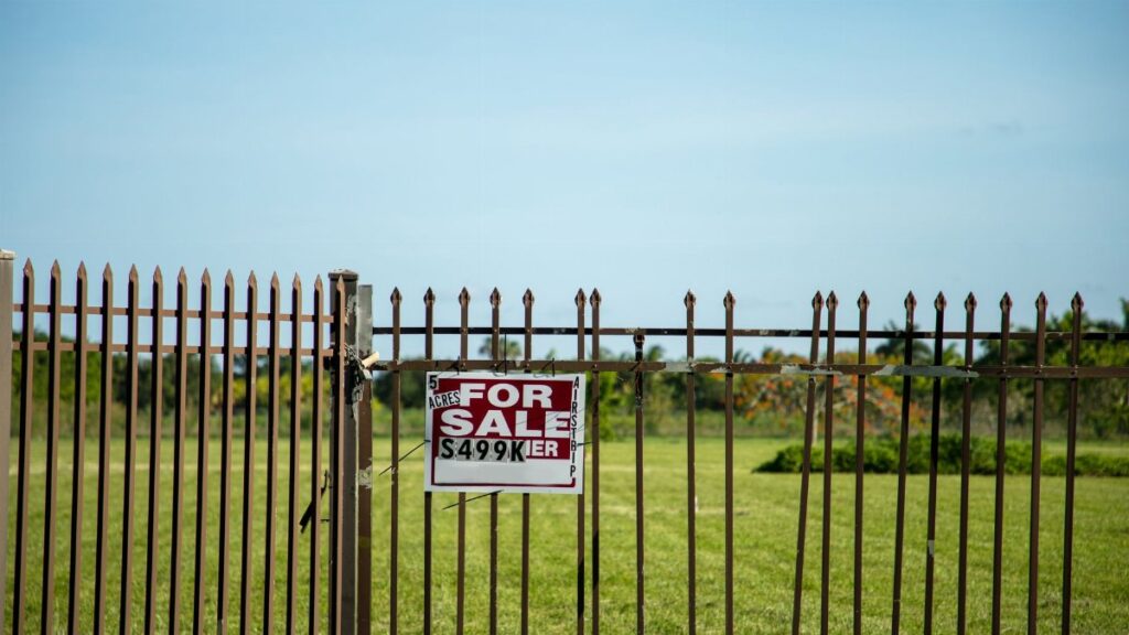 A large plot of land bordered by an iron fence, complete with a 'For Sale' sign in Miami, FL. Ideal for development.