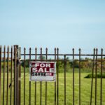 A large plot of land bordered by an iron fence, complete with a 'For Sale' sign in Miami, FL. Ideal for development.