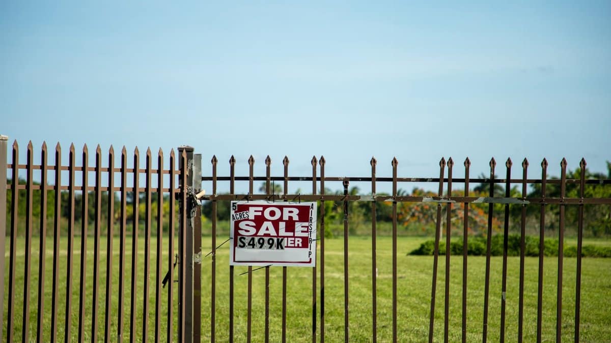A large plot of land bordered by an iron fence, complete with a 'For Sale' sign in Miami, FL. Ideal for development.