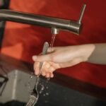 A hand washes a fork under a running water tap in a modern kitchen setting. Cleanliness concept.