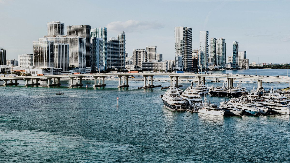 A scenic view of Miami skyline and marina, showcasing luxury yachts and modern skyscrapers under a clear blue sky.