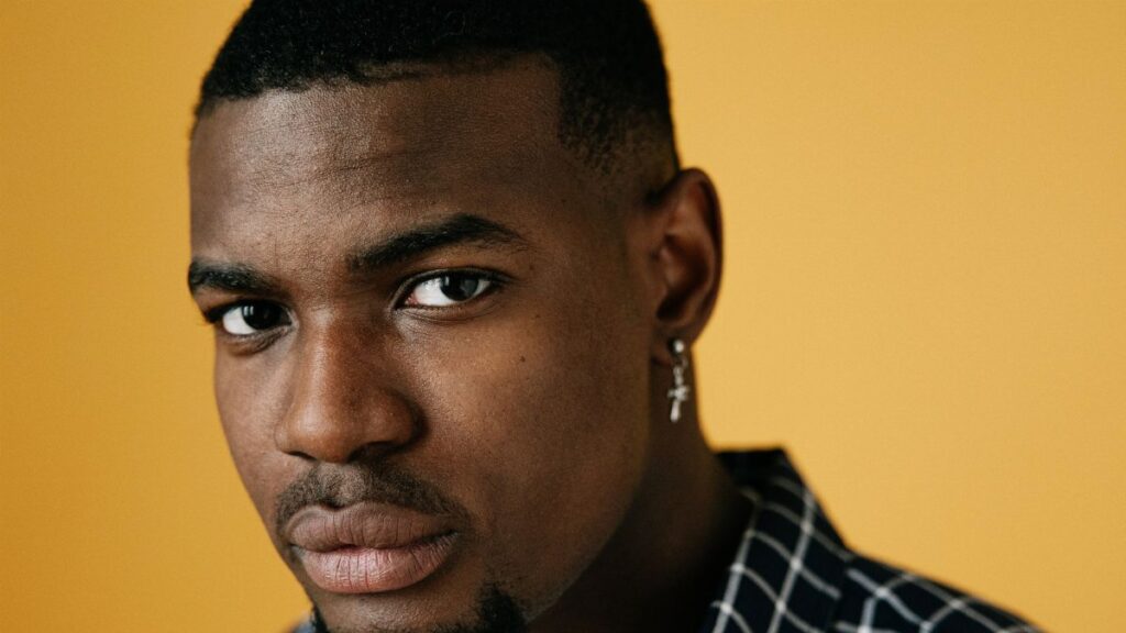 Close-up portrait of a serious man with earring against a vibrant yellow backdrop.