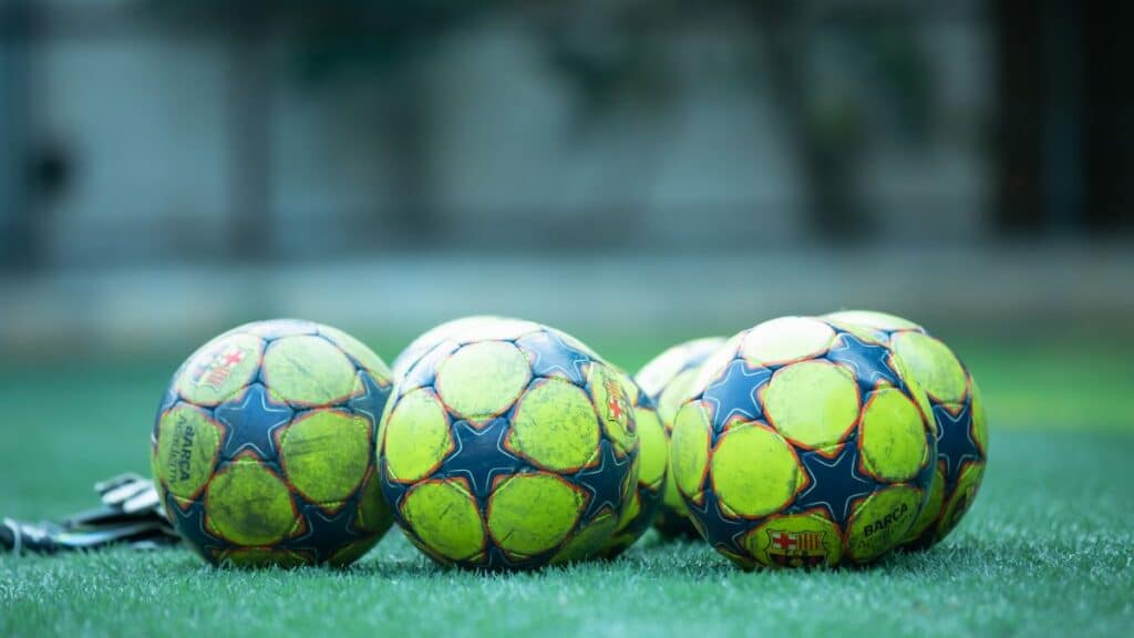 Four vibrant soccer balls resting on a green grass field.