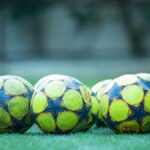 Four vibrant soccer balls resting on a green grass field.