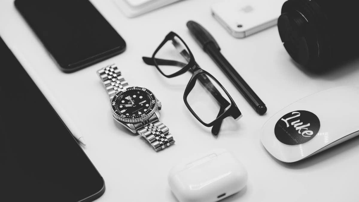Flat lay of gadgets including a watch, smartphone, glasses, and more on a white surface.