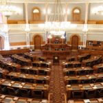 Wide view of an ornate legislative chamber with empty seats and chandeliers.
