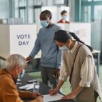 A diverse group of adults casting votes indoors on election day, maintaining safety protocols.