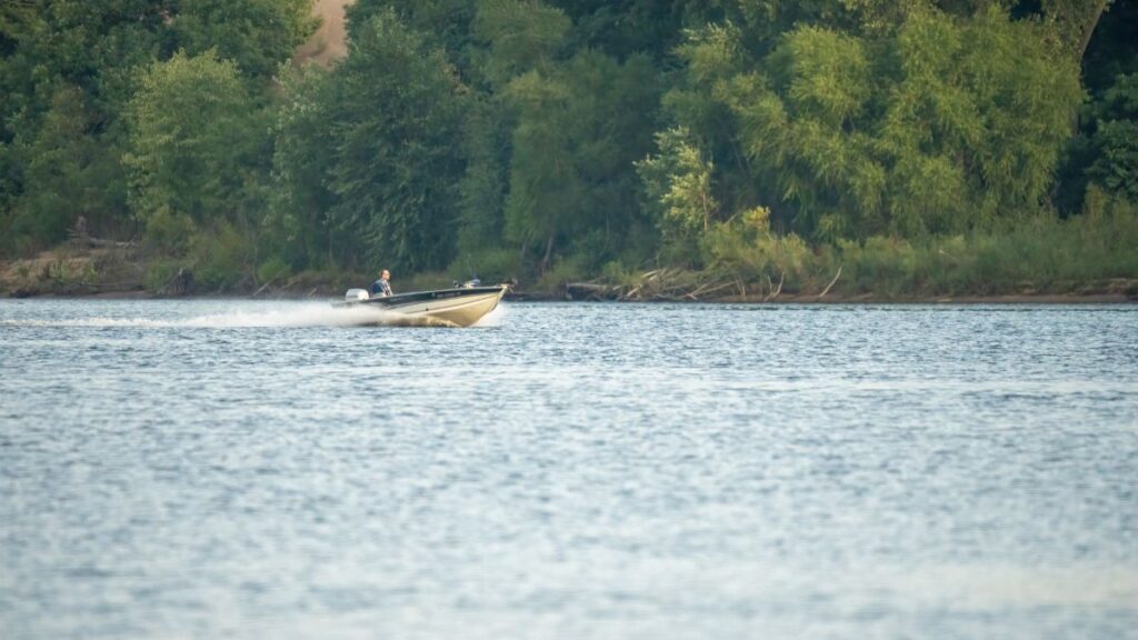 A speed boat cruising on the Mississippi River near wooded banks in Reads Landing, MN.