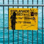 Yellow esplanade closure sign with graffiti on a metal railing by the waterfront in New York City.