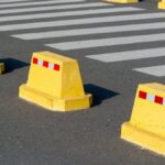 Yellow concrete barriers on asphalt next to a zebra crossing, emphasizing urban street safety.