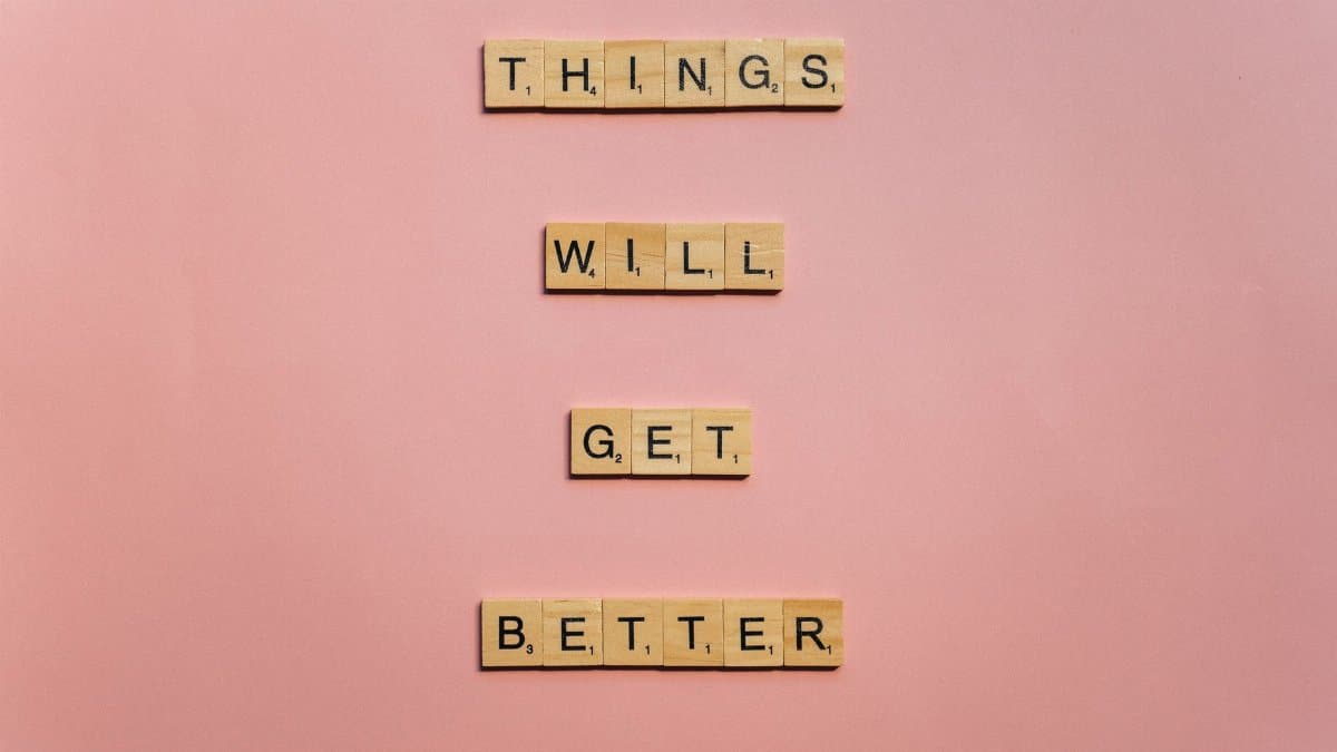 Inspirational words 'Things will get better' arranged in Scrabble tiles against a pink backdrop.