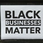 A poster advocating support for Black-owned businesses displayed on a textured wall.