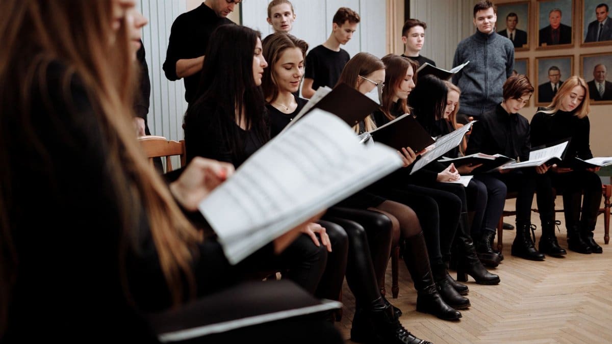 A choir rehearses indoors, focusing on music sheets for performance practice.