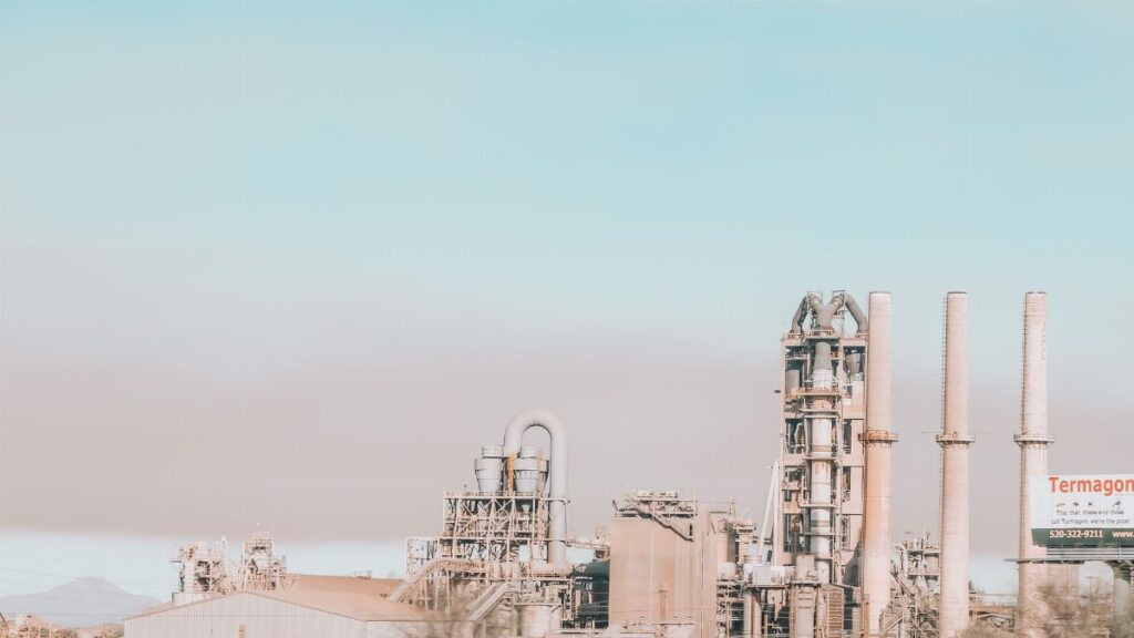 Power plant with similar stone chimneys and pipes near construction under colorful sky in city