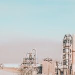 Power plant with similar stone chimneys and pipes near construction under colorful sky in city