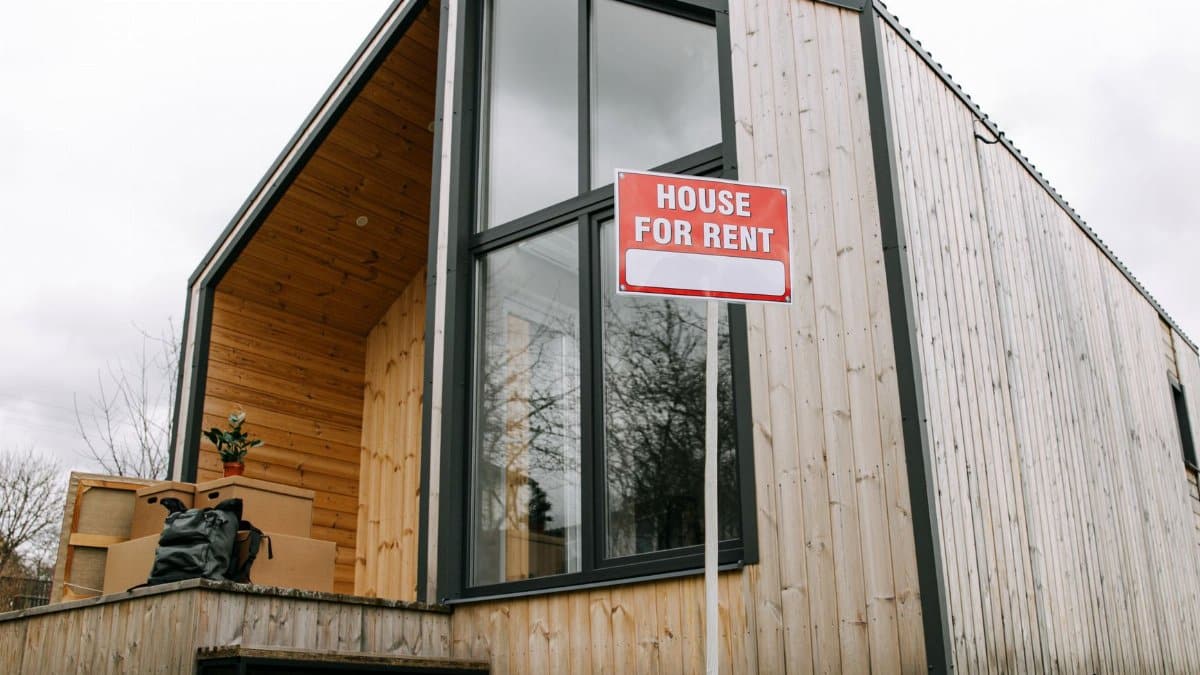 Low-angle view of a modern wooden house with a 'House for Rent' sign, showcasing contemporary architecture.