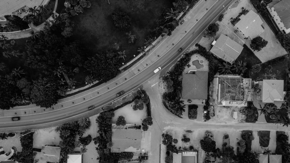 Black and white aerial photo of a residential neighborhood with a curving roadway and vehicles.