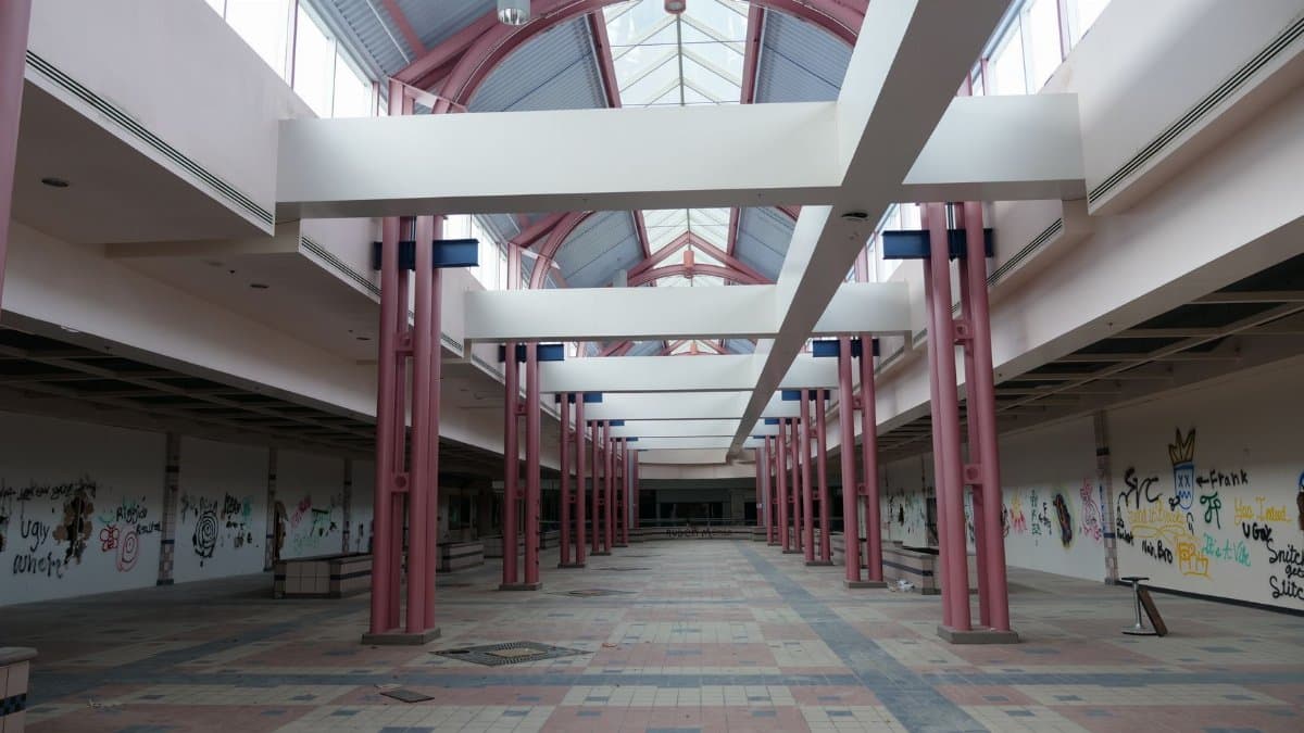 Desolate interior of an abandoned shopping mall with graffiti-covered walls.