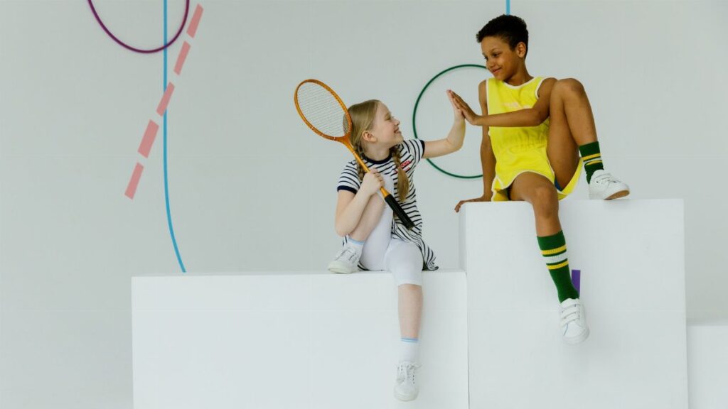 Two children having fun indoors with tennis gear. High-five moment.